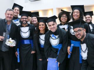 Formandos de beca e capelo reunidos com um professor em cerimônia de colação de grau da Faculdade UCL